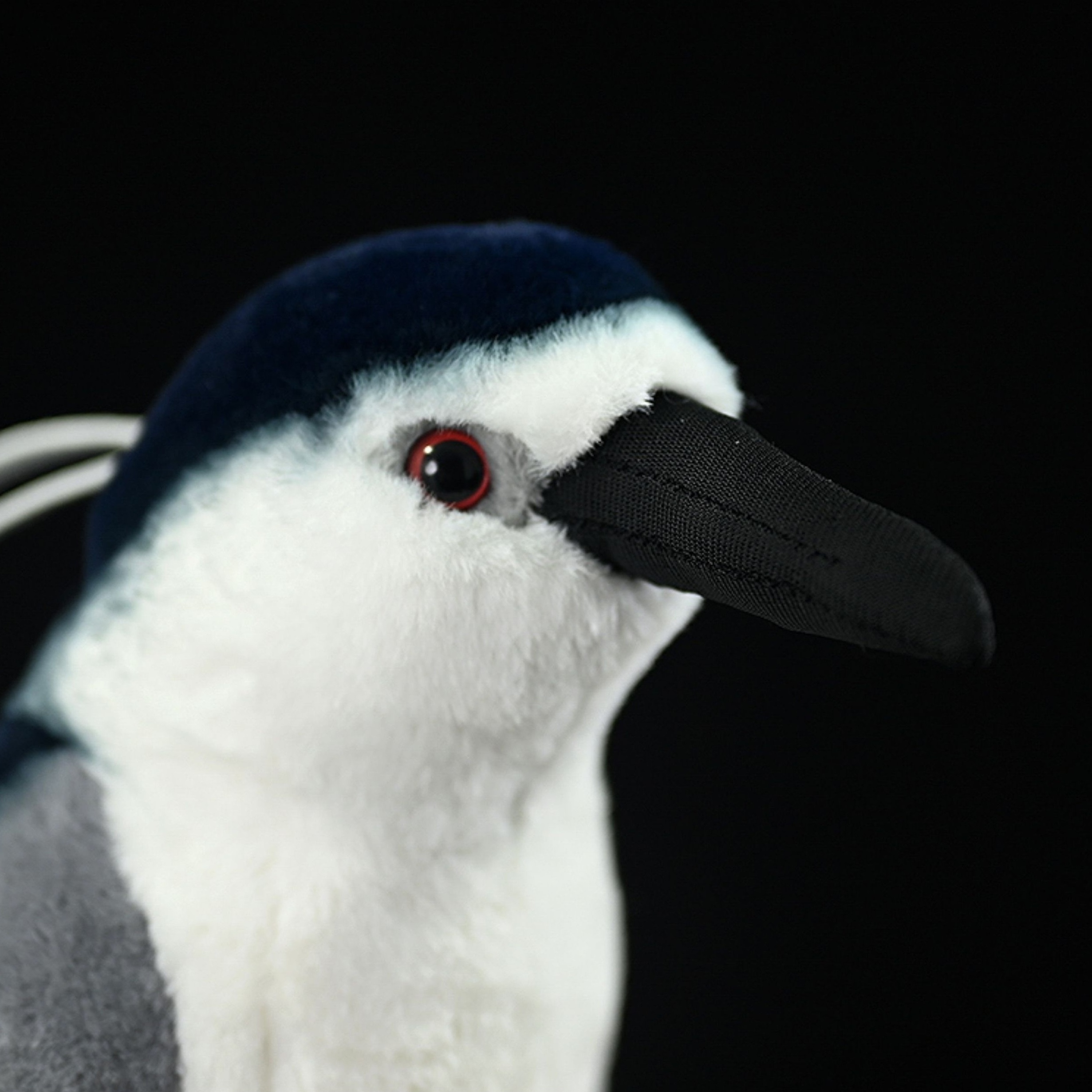 Detailed close-up of a Black-crowned Night Heron plush toy face, showcasing red eyes and a soft black beak