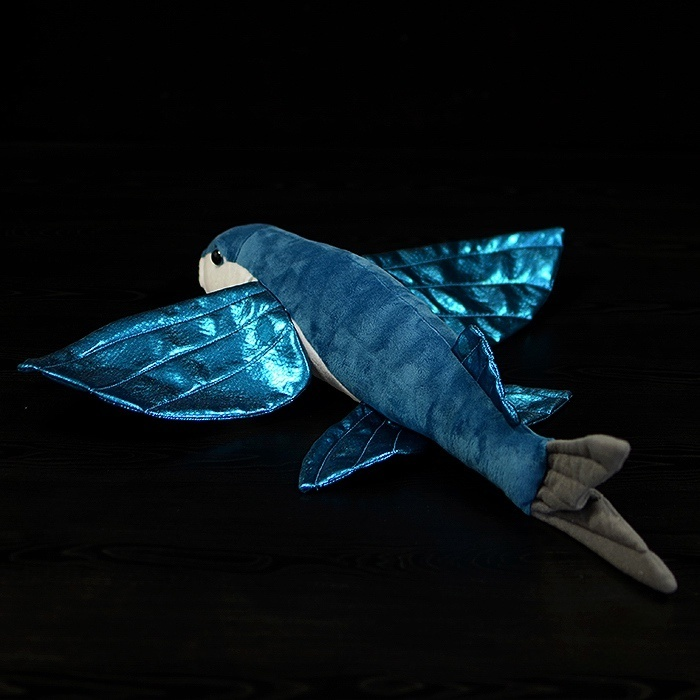 Overhead view of a four-winged flying fish plush toy with vibrant, shimmering fins