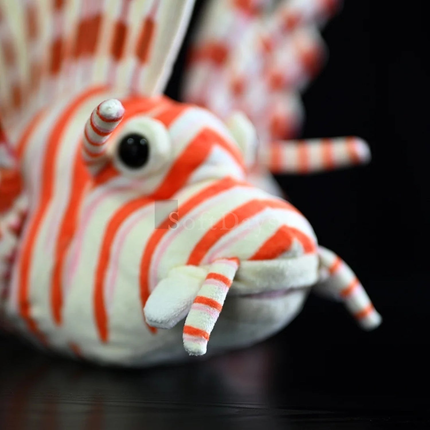 Close-up of lifelike red lionfish plush toy's face, showing detailed eyes and striped features