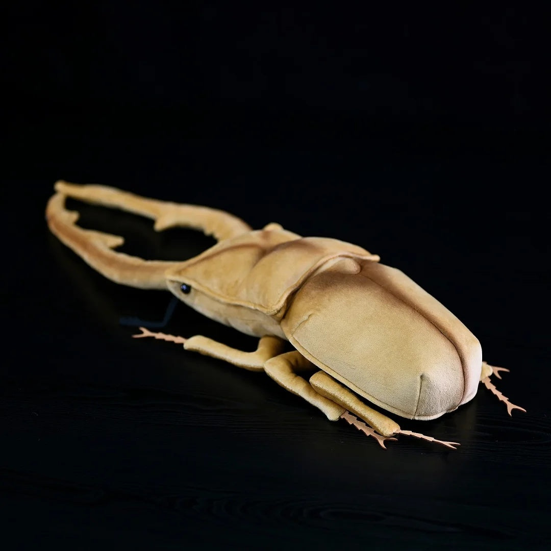Une peluche de lucane cerf-volant doré métallisé posée sur une surface noire, mettant en valeur son design inspiré des insectes.