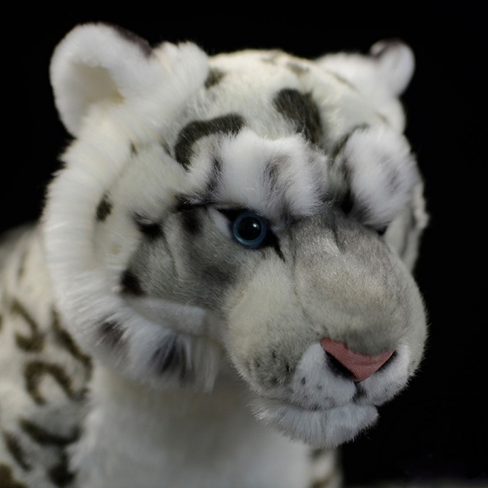 Close-up of snow leopard plush toy's face, featuring realistic blue eyes and soft fur