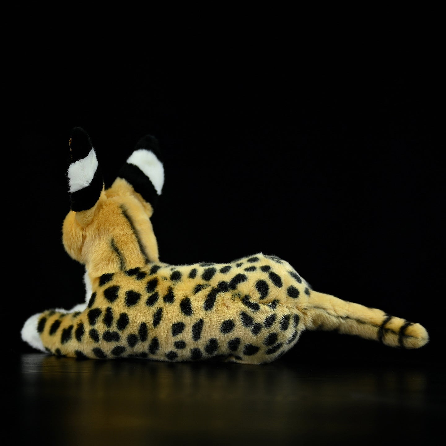 Rear view of a serval cat plush toy, highlighting its detailed spots and black-tipped tail
