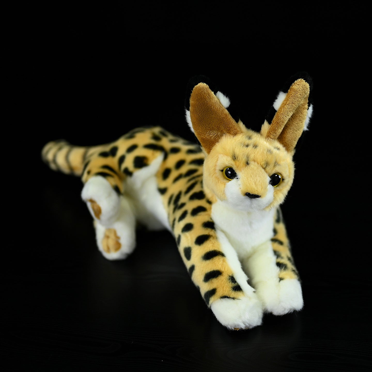 Lifelike serval cat plush toy lying down, featuring realistic spotted fur, large ears, and a soft texture