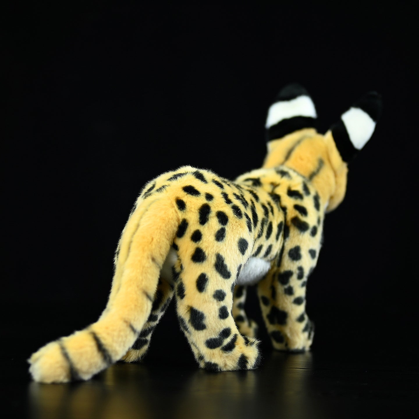 Back angle of a standing serval cat plush toy highlighting its detailed spots and striped tail