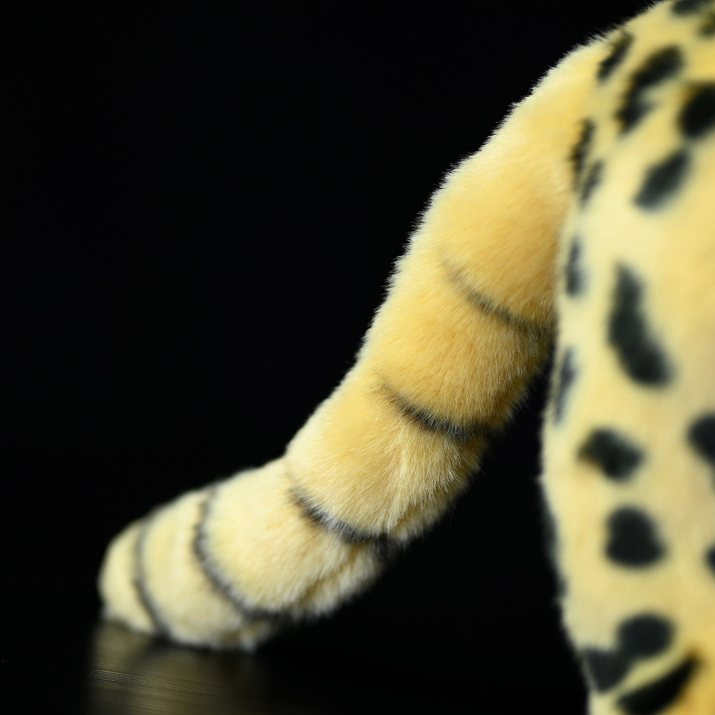 Close-up of the striped tail of a standing serval cat plush toy, emphasizing its realistic design