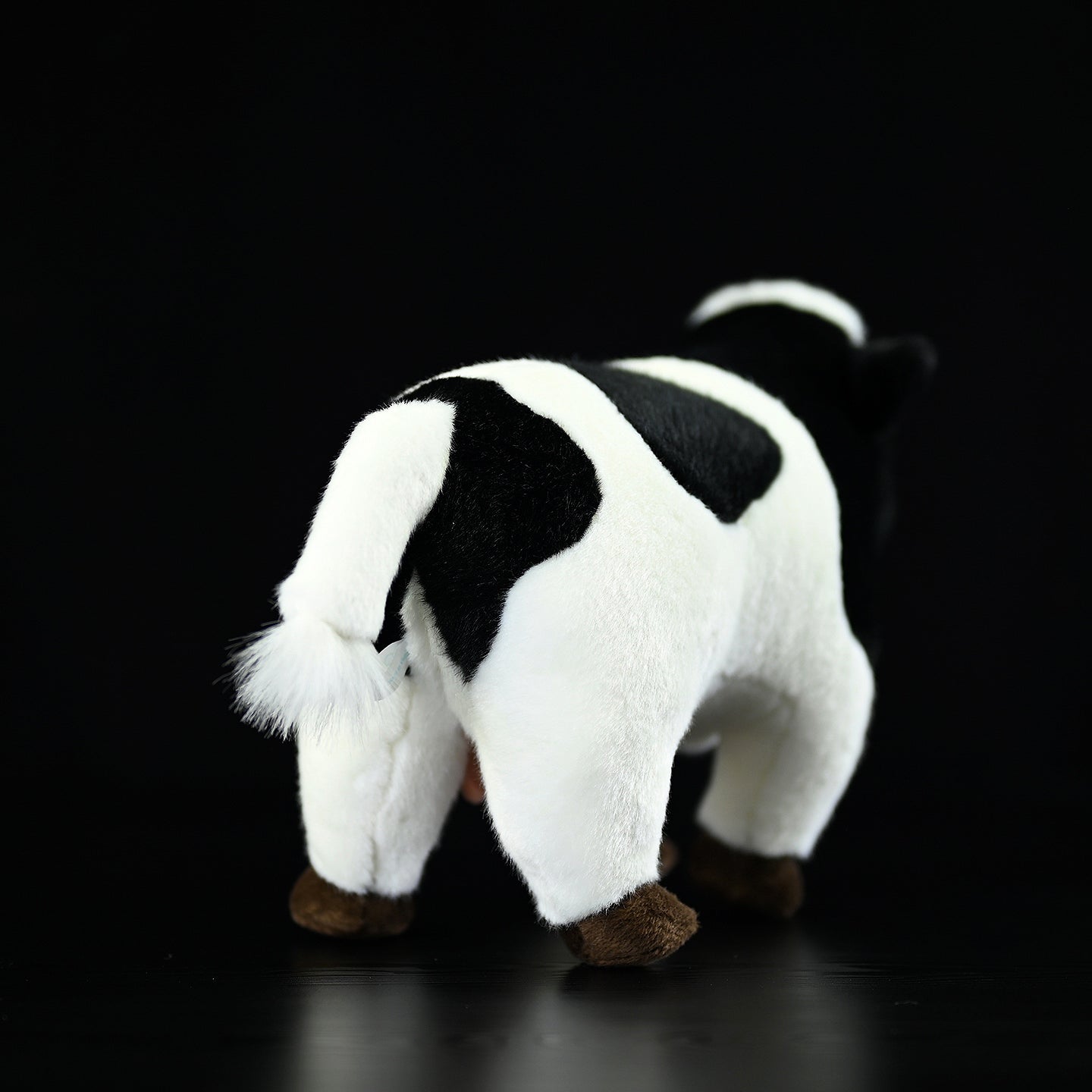 Back view of a plush Holstein cow toy, showcasing its tail and realistic black-and-white design
