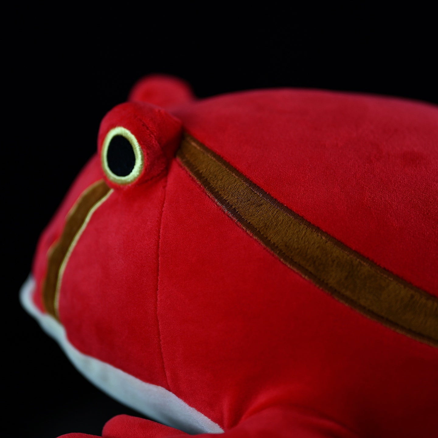 Side detail of lifelike tomato frog plush, focusing on its seamless stitching and vibrant, nature-mimicking tones