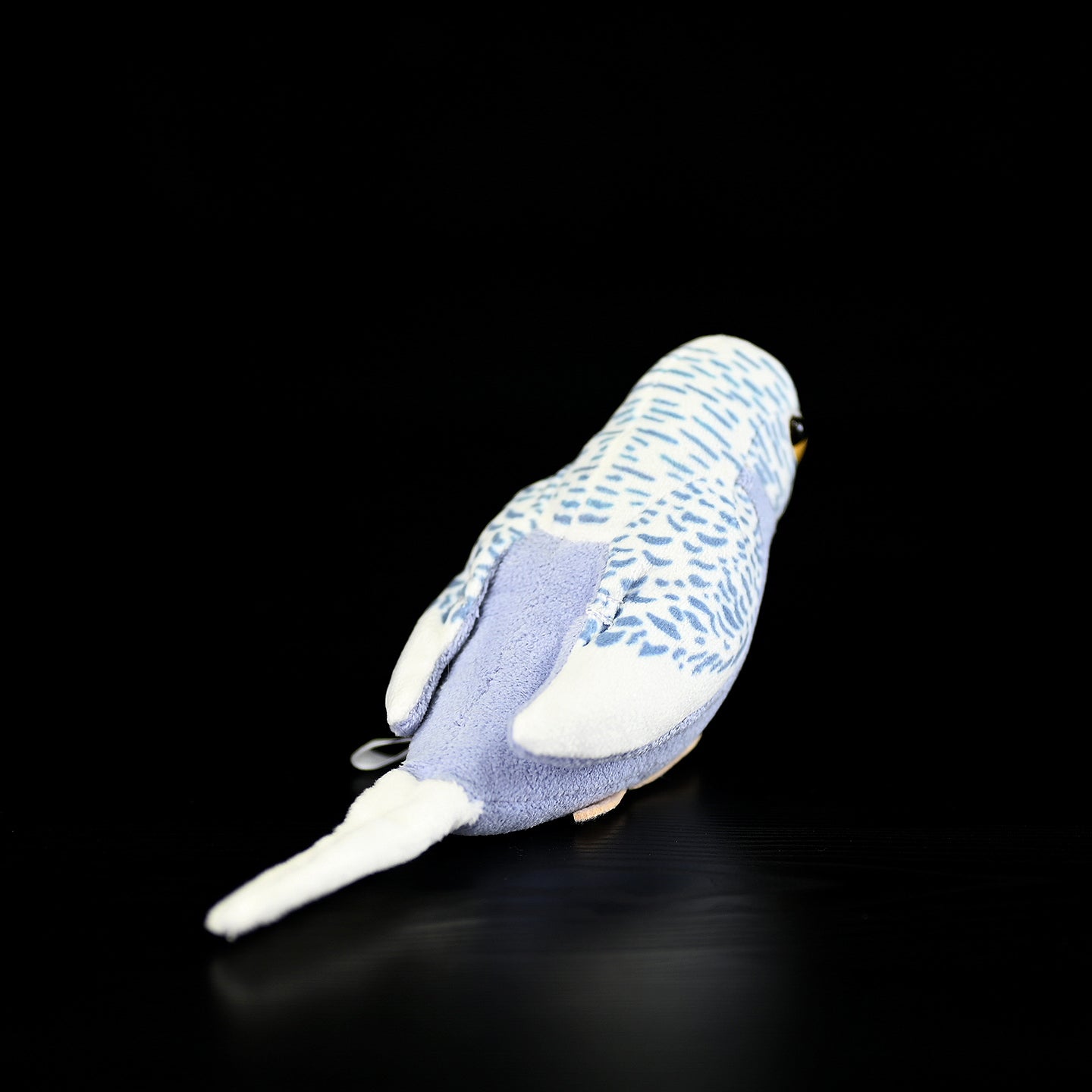 Back view of a violet budgerigar plush toy, highlighting its detailed tail and wing design