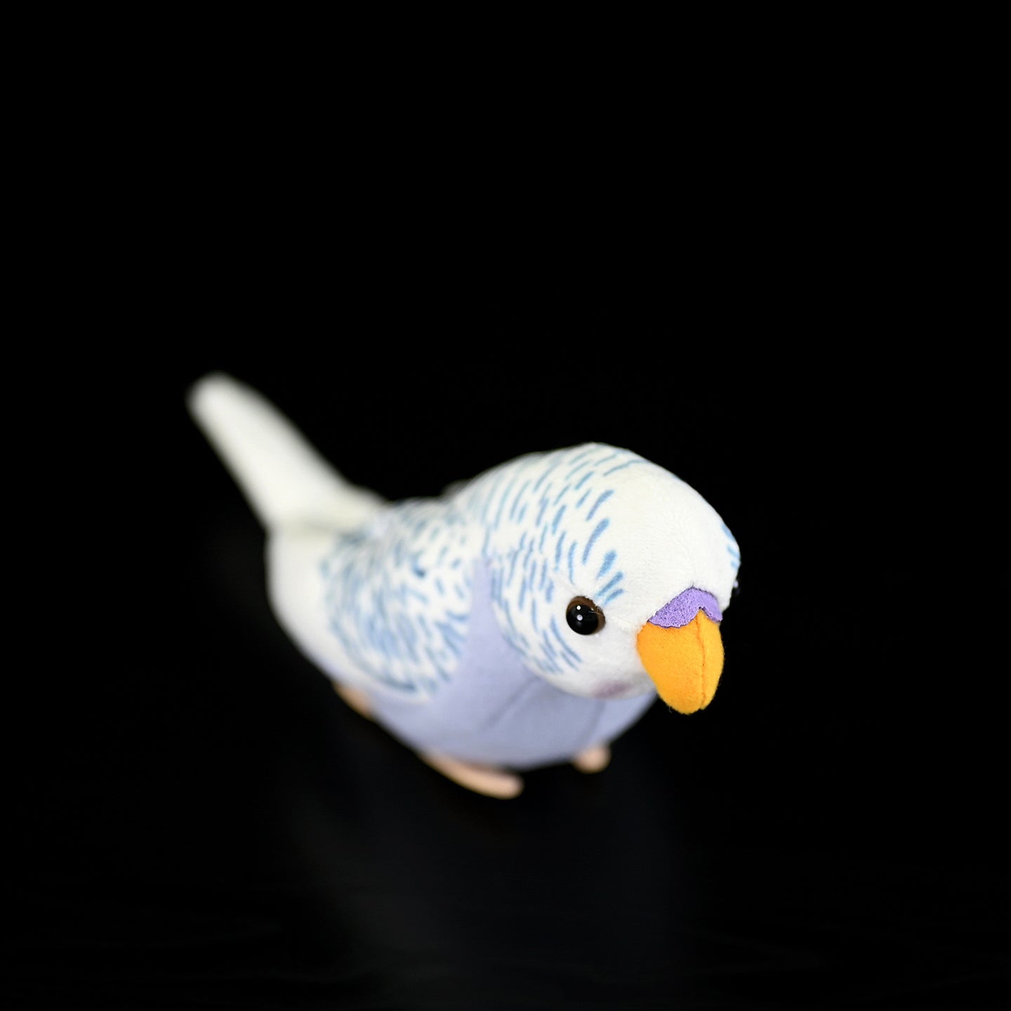Top-down view of a violet budgerigar plush toy, emphasizing its realistic markings and soft fabric