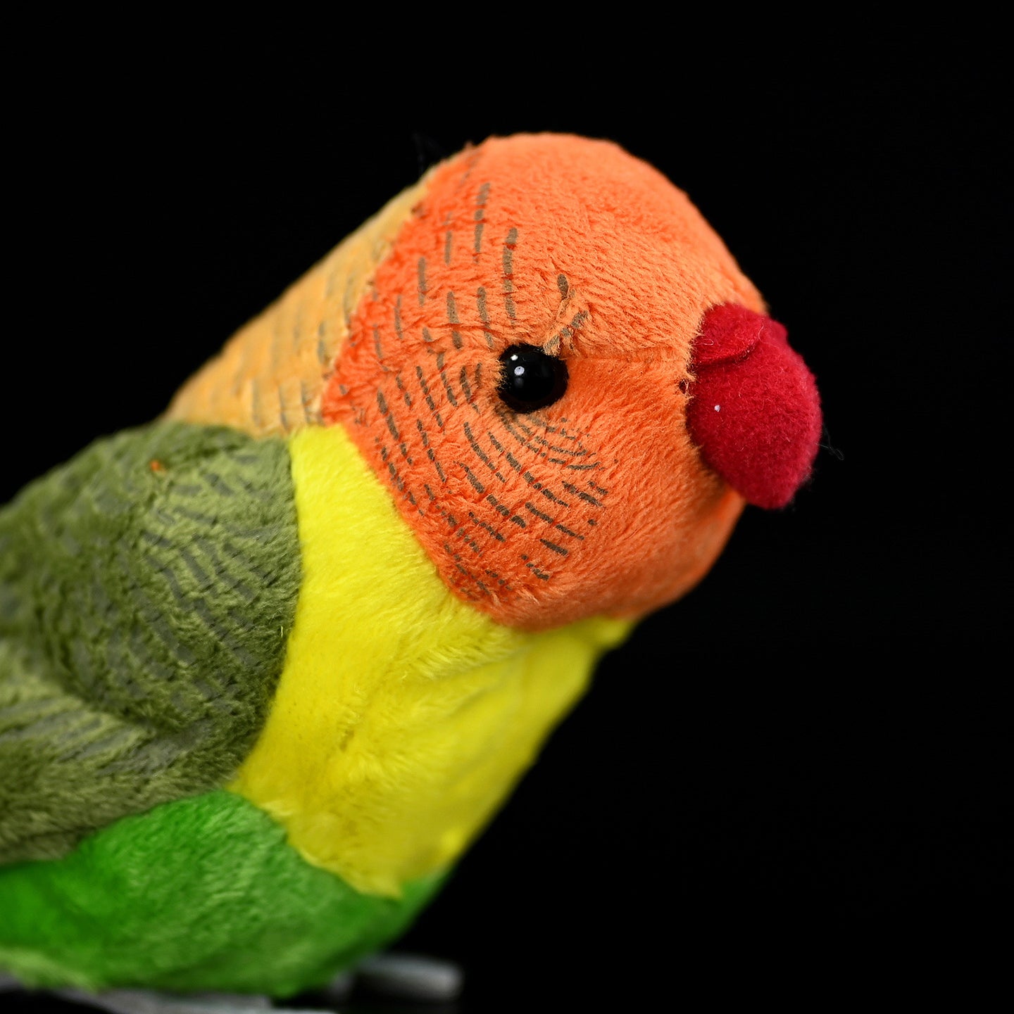 Close-up of the Lilian's lovebird plush toy's orange face and red beak, showcasing intricate details