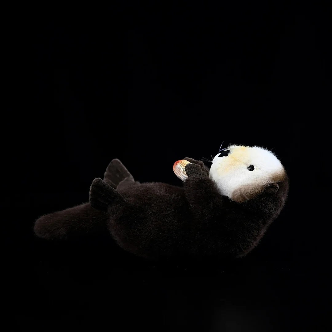 Side profile of lifelike SoftDaysLab® sea otter plush holding a clam, featuring embroidered facial details