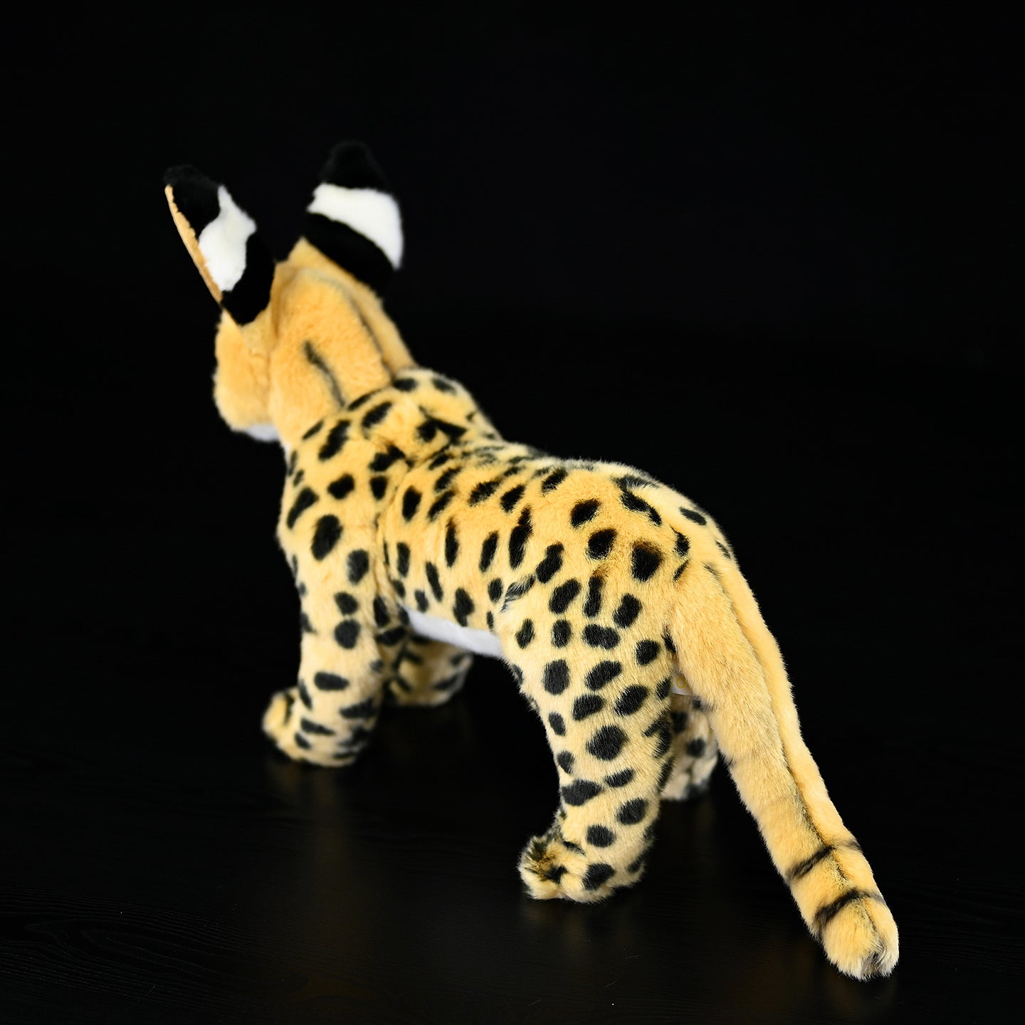 Rear view of a standing serval cat plush toy with black-tipped ears and a realistic spotted coat