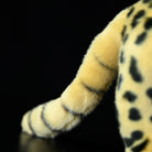 Close-up of the striped tail of a standing serval cat plush toy, emphasizing its realistic design