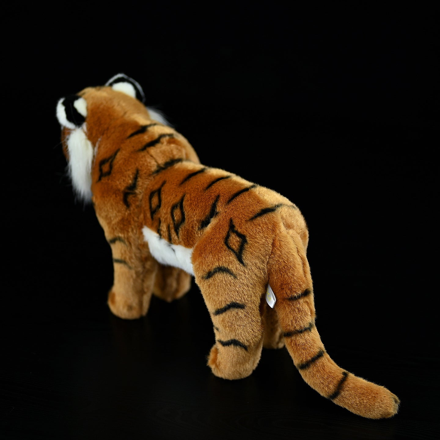 Back view of a realistic tiger plush toy, featuring its detailed fur and lifelike tail