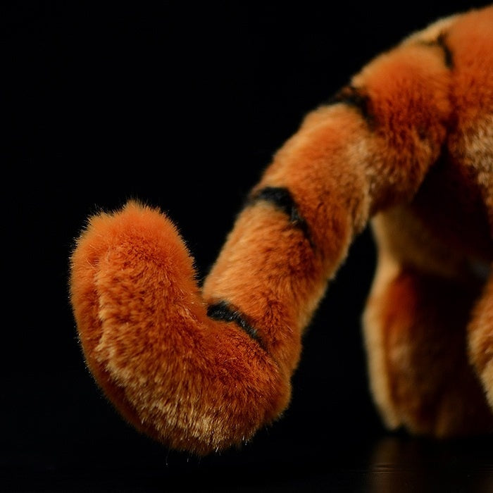 Close-up of a tiger cub plush toy's curved tail, showcasing lifelike black stripes and soft orange fur