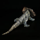 Rear view of a frilled lizard plush, emphasizing its long, textured tail and detailed reptile-like design